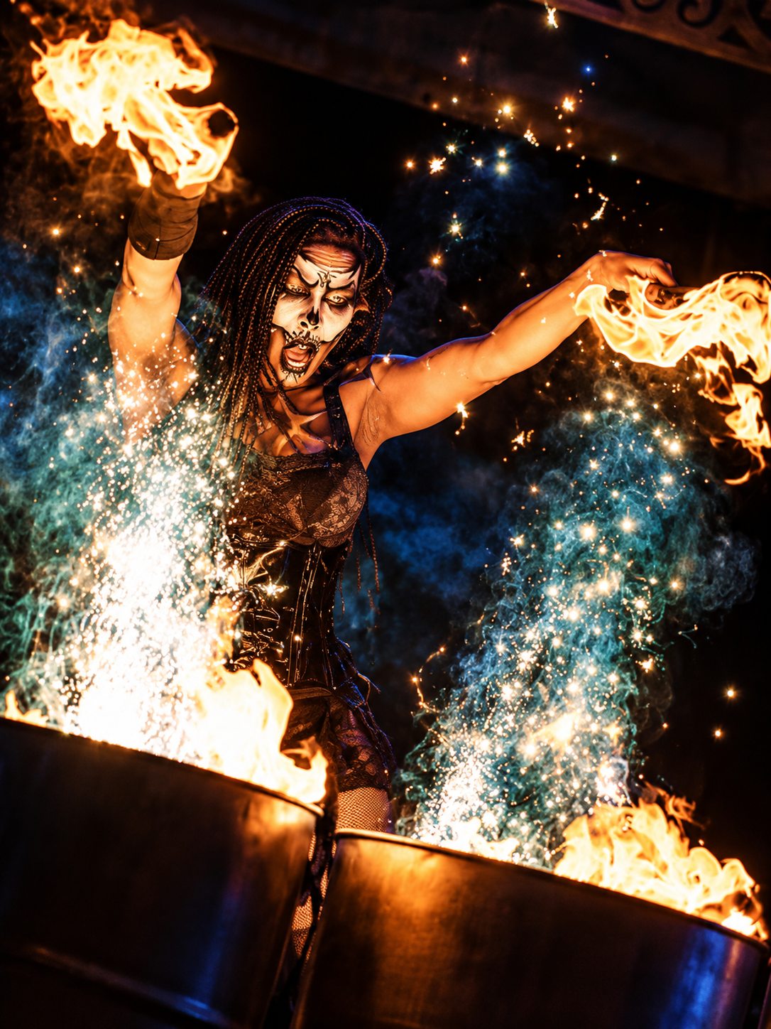Tiana Powell as Maman Brigitte reaches over the fire barrels in a shower of sparks — Voodoo: Bayou's Edge, Knott's Scary Farm 2026