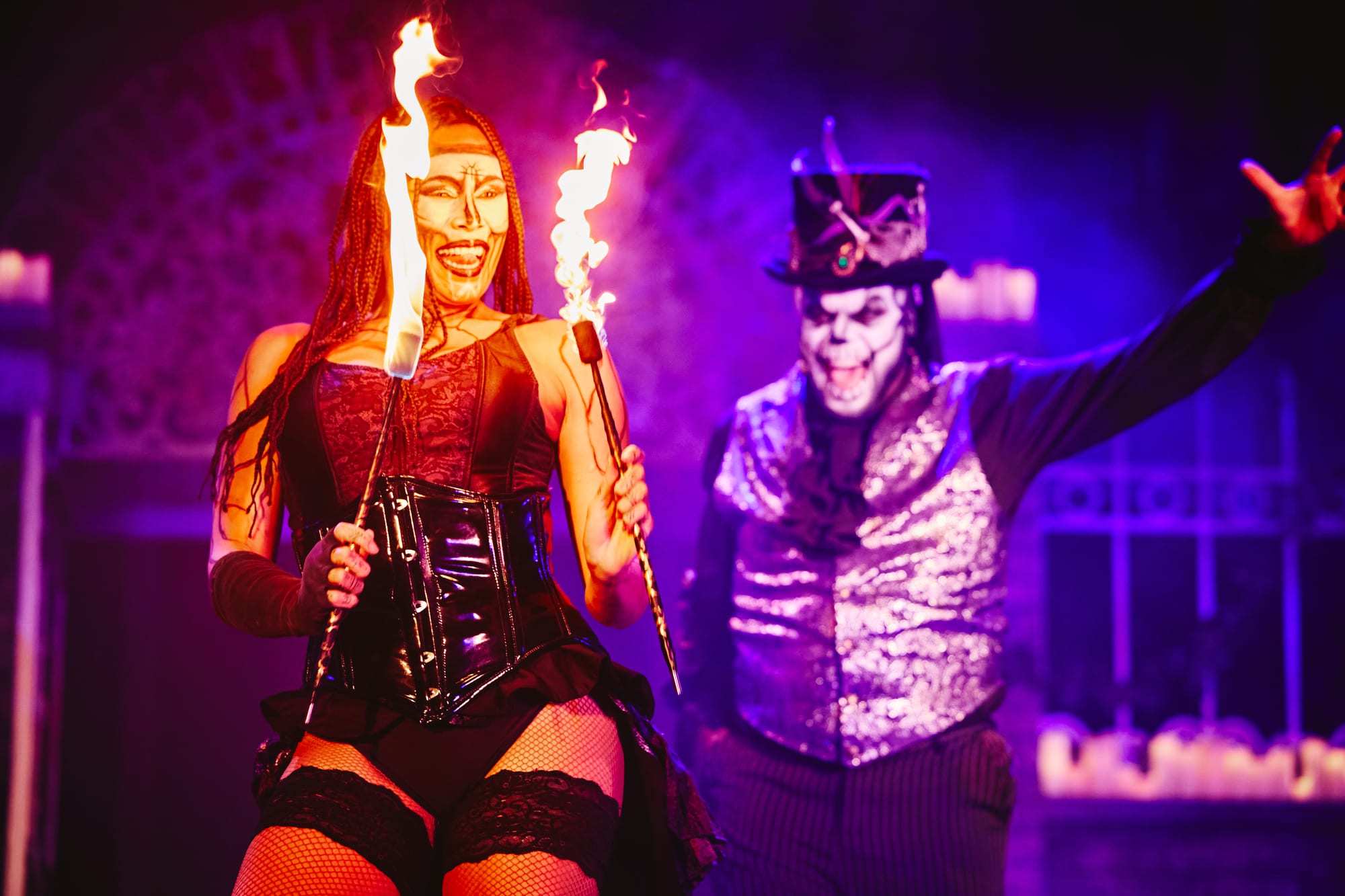Maman Brigitte lifts two torches as Dedrick Bonner's Baron Samedi throws his arm wide behind her — Voodoo: Bayou's Edge, Knott's Scary Farm 2026
